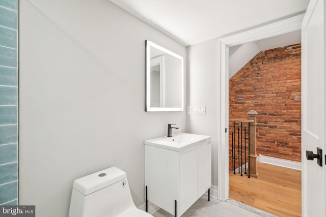 bathroom with toilet, brick wall, wood finished floors, vanity, and baseboards