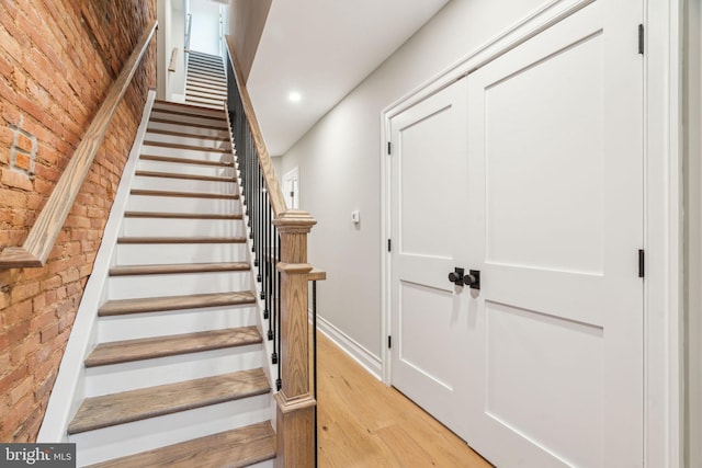 stairway with recessed lighting, baseboards, brick wall, and wood finished floors