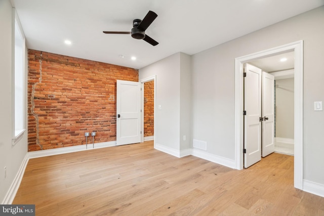 unfurnished bedroom with brick wall, visible vents, baseboards, and light wood finished floors