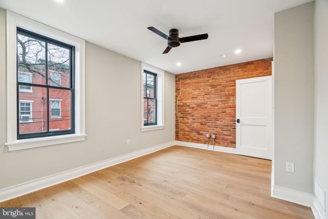 unfurnished room featuring ceiling fan, brick wall, baseboards, and light wood-style flooring