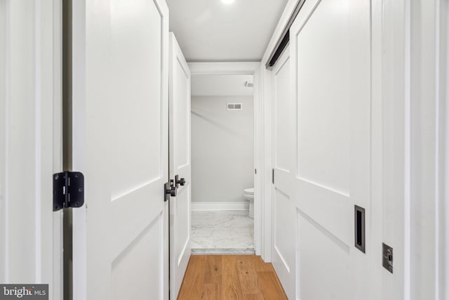 hall with light wood finished floors, visible vents, and baseboards