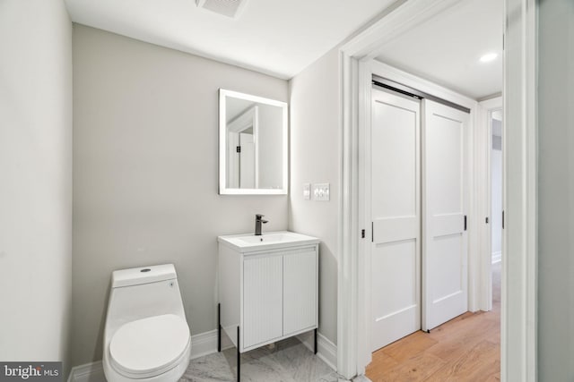 half bath with toilet, vanity, visible vents, and baseboards