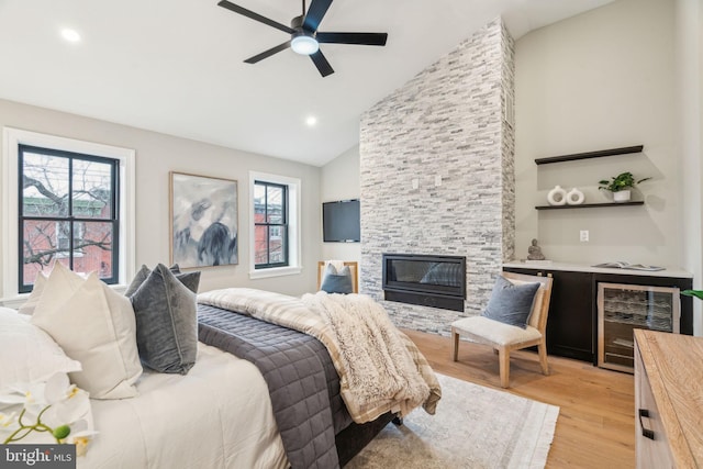 bedroom with a stone fireplace, wine cooler, a ceiling fan, light wood-style floors, and a bar