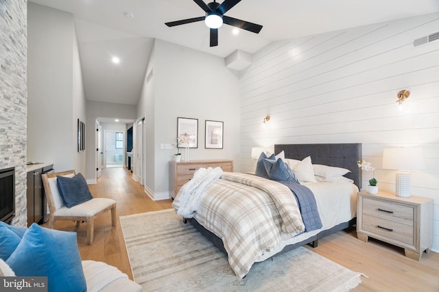 bedroom featuring high vaulted ceiling, visible vents, a fireplace, and light wood-style flooring