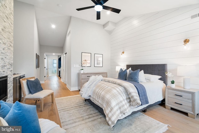 bedroom with baseboards, visible vents, light wood-type flooring, a fireplace, and high vaulted ceiling