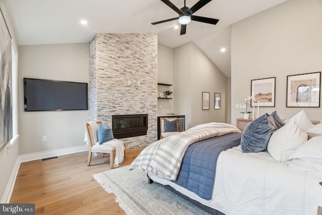 bedroom featuring light wood finished floors, baseboards, visible vents, vaulted ceiling, and a stone fireplace