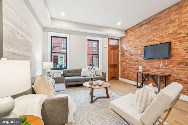 living area featuring light wood-style floors, baseboards, and brick wall