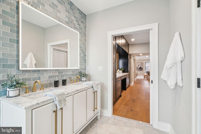 ensuite bathroom with double vanity, baseboards, decorative backsplash, and a sink