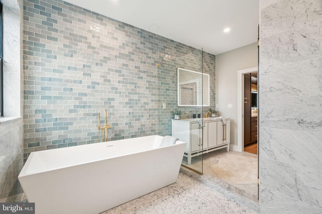 full bath with tile walls, recessed lighting, a soaking tub, vanity, and speckled floor