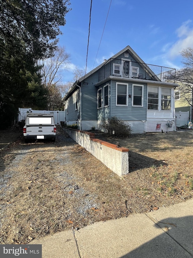 view of side of property featuring driveway, a balcony, and fence