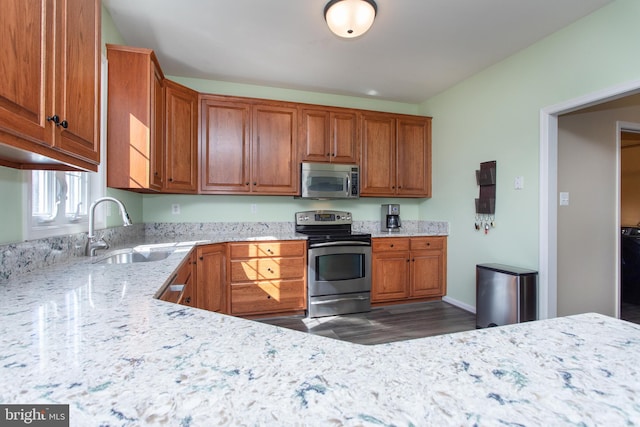 kitchen with stainless steel appliances, brown cabinetry, a sink, and light stone counters