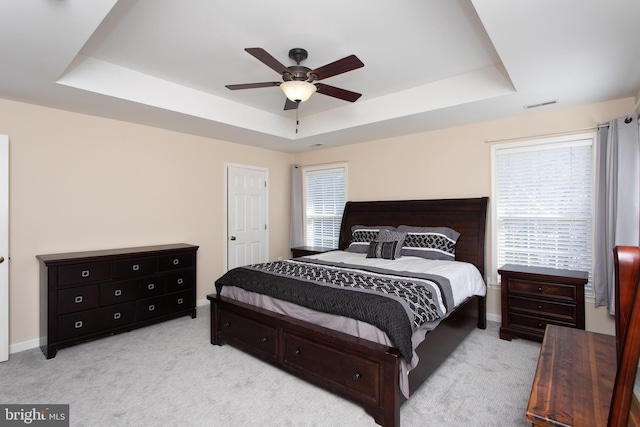 bedroom with baseboards, visible vents, a raised ceiling, and light colored carpet