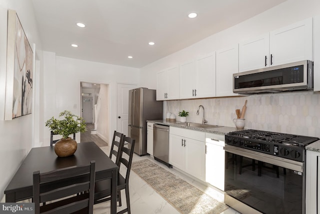 kitchen featuring appliances with stainless steel finishes, a sink, white cabinets, and decorative backsplash