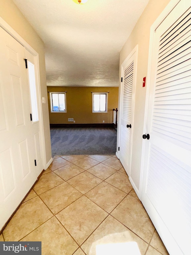 hallway featuring light carpet, baseboards, and light tile patterned flooring