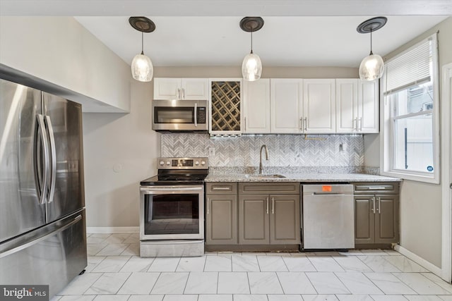 kitchen featuring light stone counters, a sink, appliances with stainless steel finishes, decorative backsplash, and decorative light fixtures