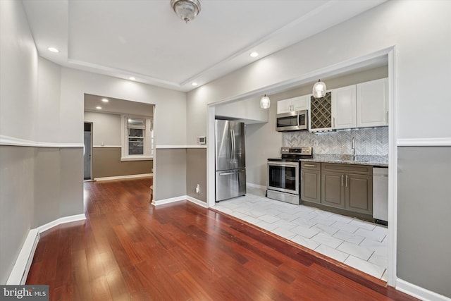 kitchen featuring appliances with stainless steel finishes, a sink, decorative backsplash, and wood finished floors