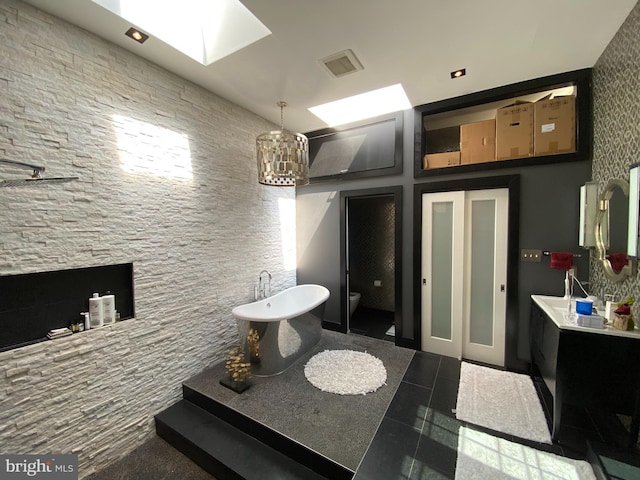 bathroom featuring a skylight, a soaking tub, an inviting chandelier, vanity, and tile patterned floors