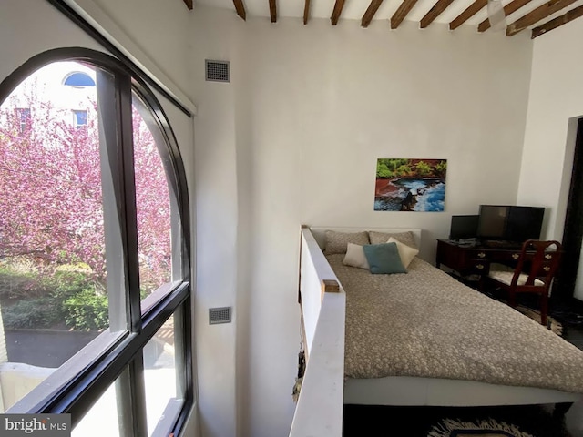 bedroom with beam ceiling, multiple windows, visible vents, and a towering ceiling