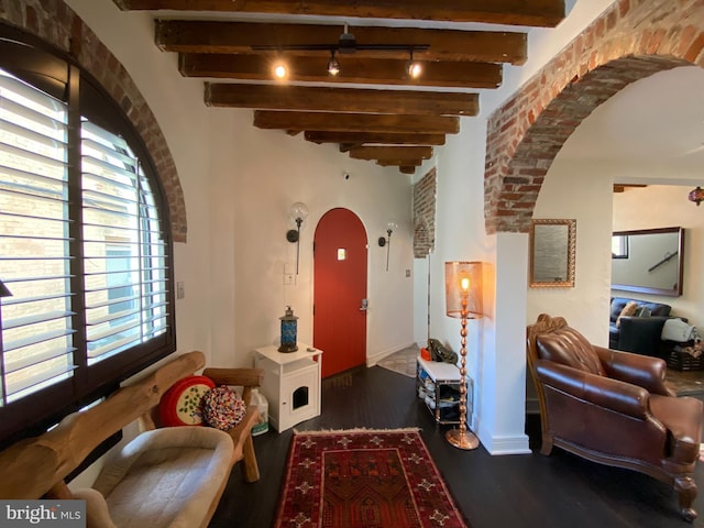 foyer entrance with track lighting, arched walkways, beamed ceiling, and wood finished floors