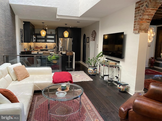 living area featuring a textured ceiling, dark wood-style flooring, arched walkways, and baseboards