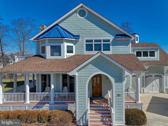 view of front of property featuring a chimney, a porch, concrete driveway, a standing seam roof, and metal roof