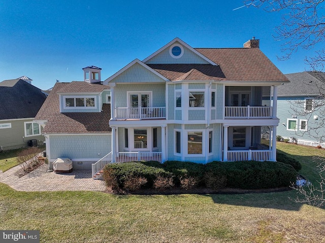 view of front of house with a chimney, a porch, a shingled roof, a front yard, and a balcony