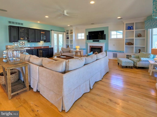 living room with light wood-style flooring, recessed lighting, visible vents, indoor wet bar, and a glass covered fireplace