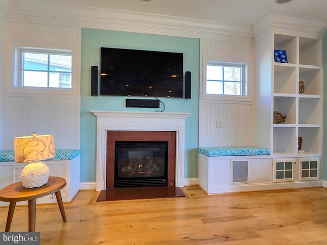 living room featuring wood finished floors, a fireplace with flush hearth, and crown molding