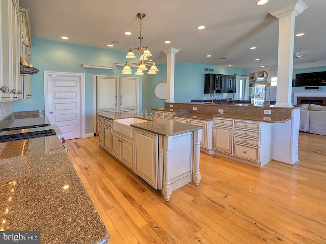 kitchen with recessed lighting, a sink, open floor plan, light wood finished floors, and decorative columns