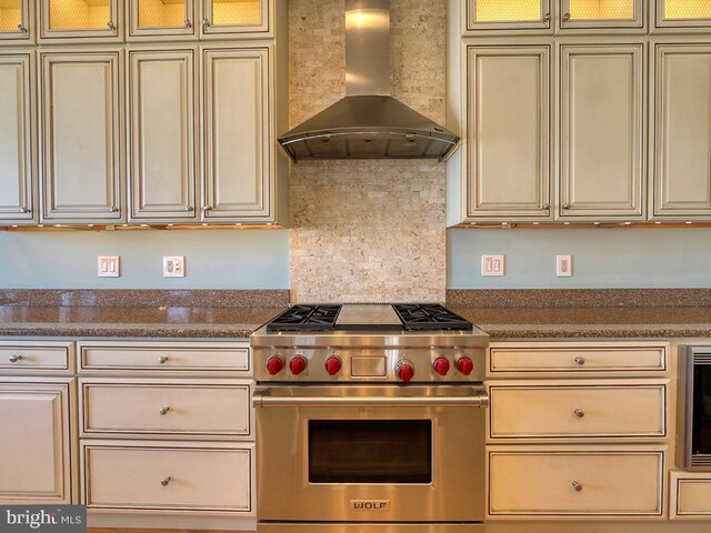 kitchen featuring dark countertops, wall chimney exhaust hood, premium range, and cream cabinetry