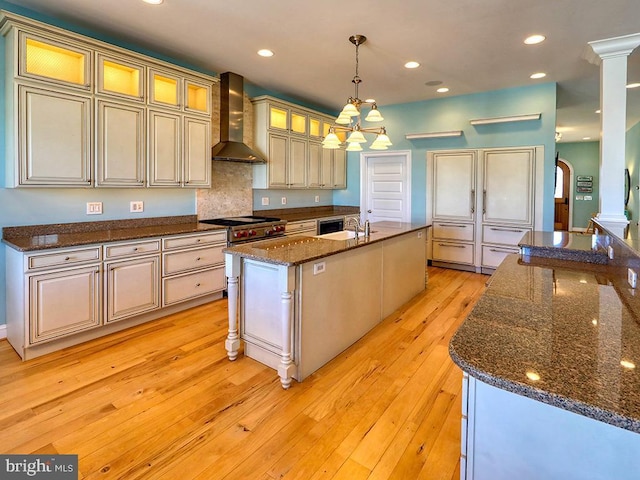 kitchen featuring arched walkways, a center island with sink, recessed lighting, light wood-style floors, and wall chimney exhaust hood