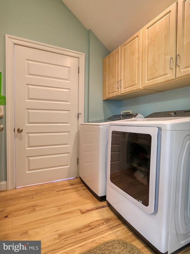 clothes washing area with light wood-type flooring, cabinet space, and washing machine and clothes dryer