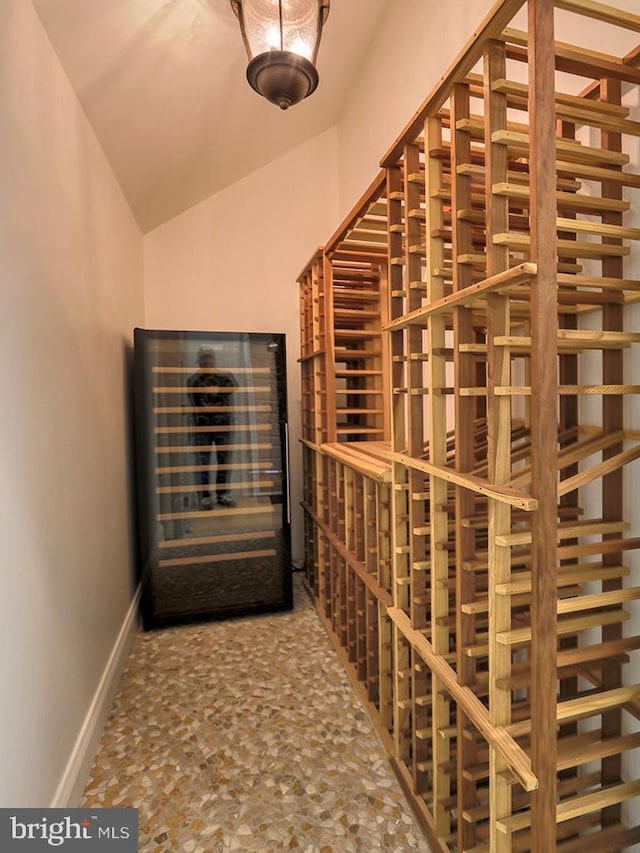 wine room featuring wine cooler, baseboards, and vaulted ceiling