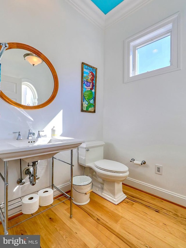 half bath featuring baseboards, wood finished floors, toilet, and crown molding