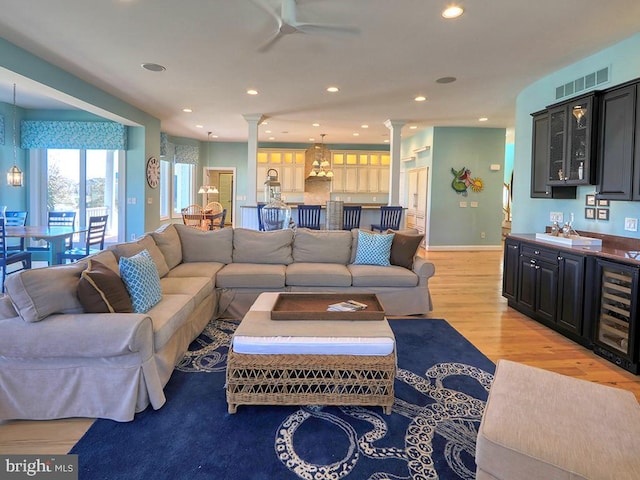 living room featuring wine cooler, bar area, visible vents, and ornate columns