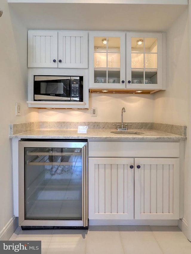 bar with wine cooler, a sink, baseboards, wet bar, and stainless steel microwave