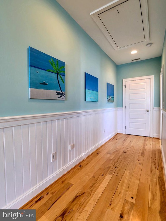 hallway with attic access, a wainscoted wall, visible vents, and hardwood / wood-style flooring