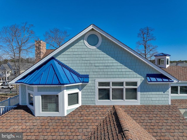 back of house featuring a standing seam roof, a chimney, and metal roof