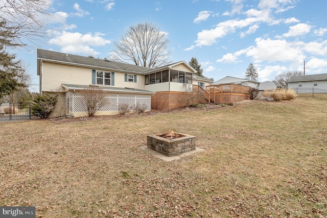 back of property with a sunroom, an outdoor fire pit, fence, and a lawn