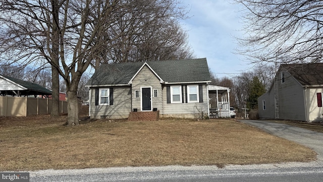 view of front of home featuring aphalt driveway, roof with shingles, fence, and a front lawn