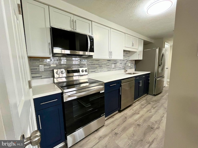 kitchen with blue cabinets, stainless steel appliances, a sink, light countertops, and light wood-type flooring