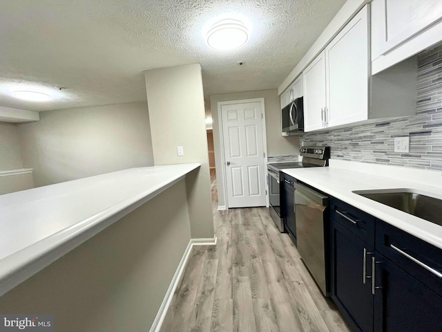 kitchen with light countertops, light wood-style flooring, decorative backsplash, appliances with stainless steel finishes, and white cabinets