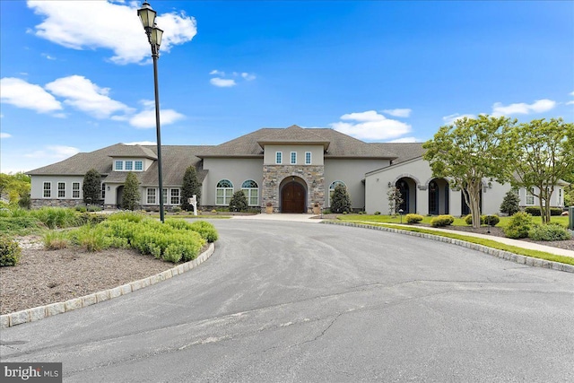 view of front of home with driveway, stone siding, and stucco siding