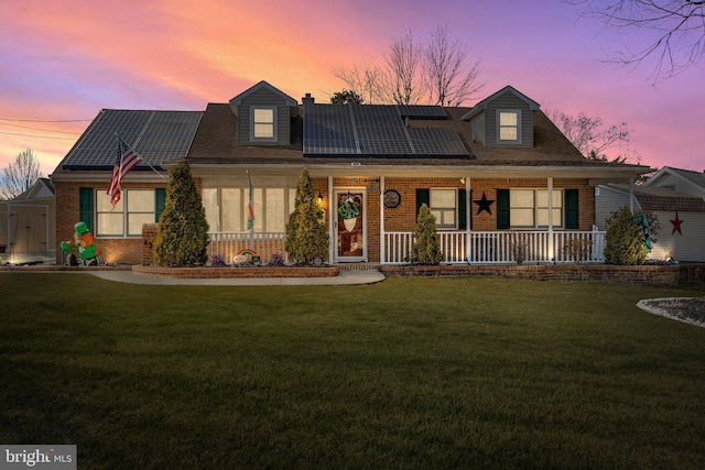 view of front of property with a porch, roof mounted solar panels, brick siding, and a lawn