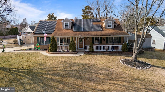 view of front of house featuring brick siding, a chimney, covered porch, roof mounted solar panels, and a front lawn