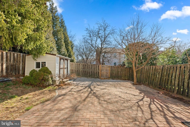 view of patio featuring an outdoor structure, a gate, a fenced backyard, and a storage unit