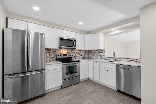 kitchen featuring a sink, stainless steel appliances, light countertops, white cabinets, and backsplash