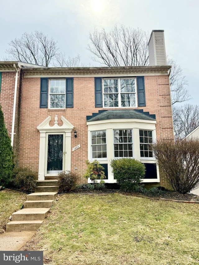 view of front of home featuring brick siding, a chimney, and a front yard