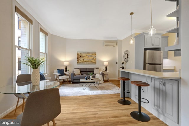 living area featuring baseboards, light wood finished floors, a wall mounted AC, and crown molding