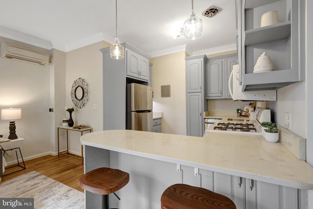 kitchen featuring a wall unit AC, visible vents, ornamental molding, freestanding refrigerator, and a peninsula